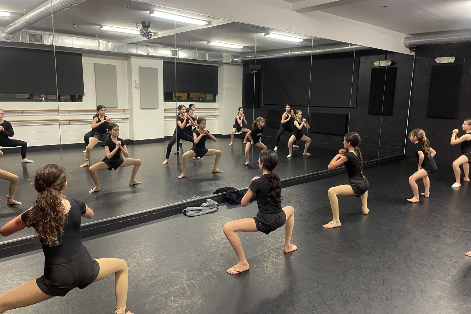 A jazz class in black tops and black shorts working in the studio mirror